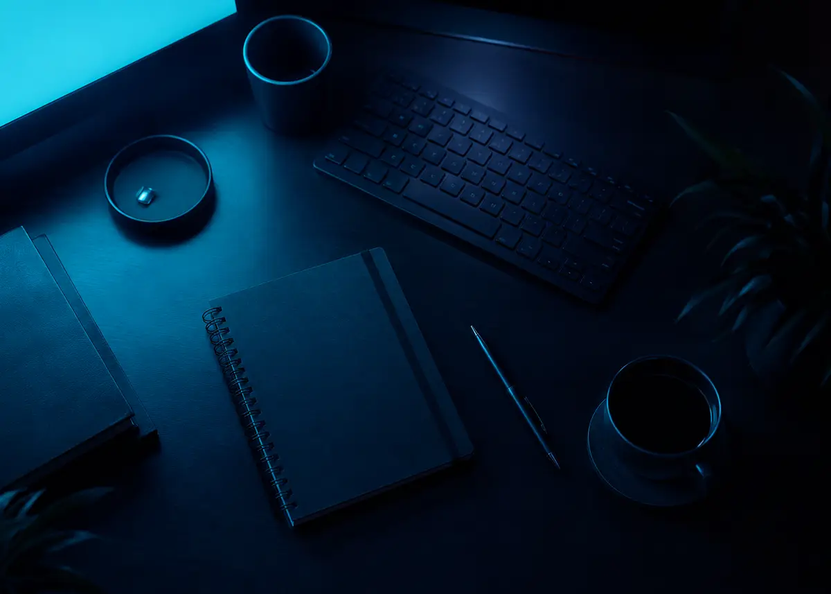 Vista cenital de un escritorio con teclado, agenda y pantalla azulada